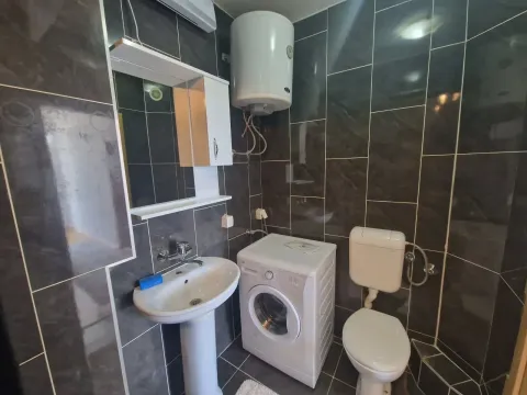 Bathroom equipped with a sink, washing machine, toilet, and dark tiles. - image 9
