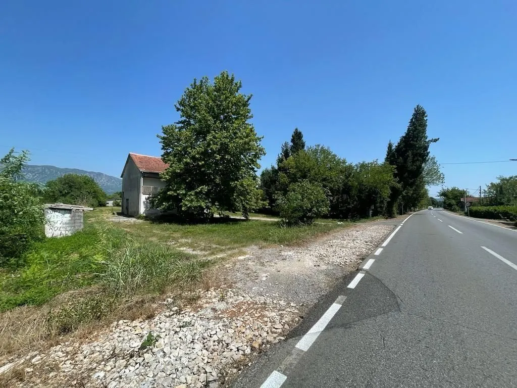 Kuća i plac pored asfaltnog puta pod vedrim nebom.