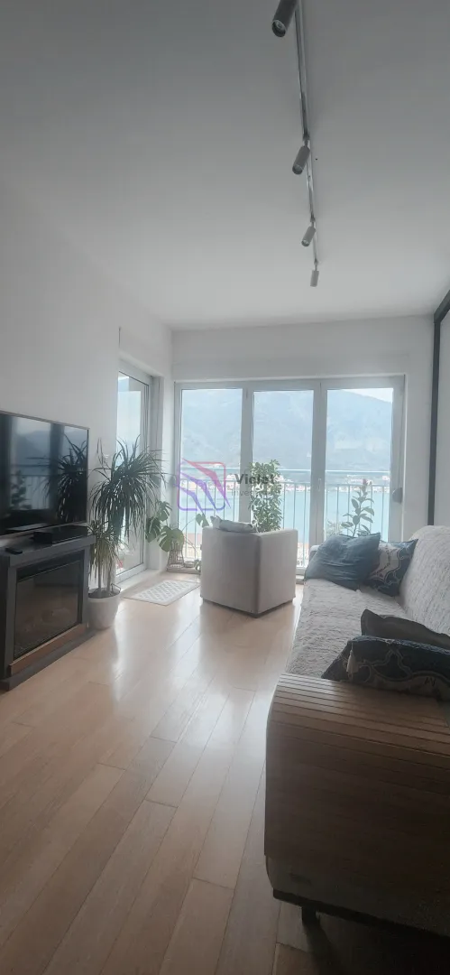 Dnevna soba sa garniturom, televizorom i pogledom na more kroz balkonska vrata.