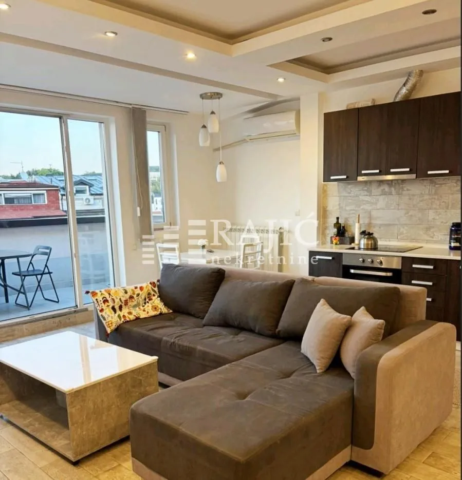 Living room with a sofa and a kitchen in the background.