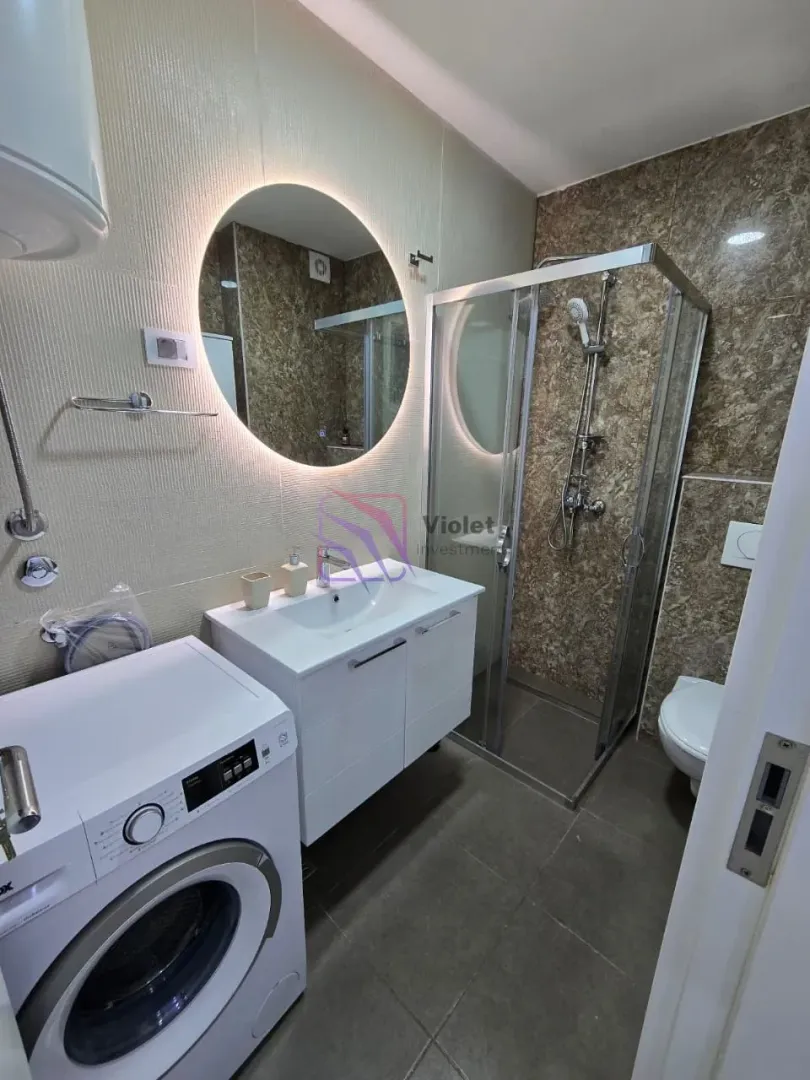 Modern bathroom with a shower cabin, washbasin, mirror, and washing machine.