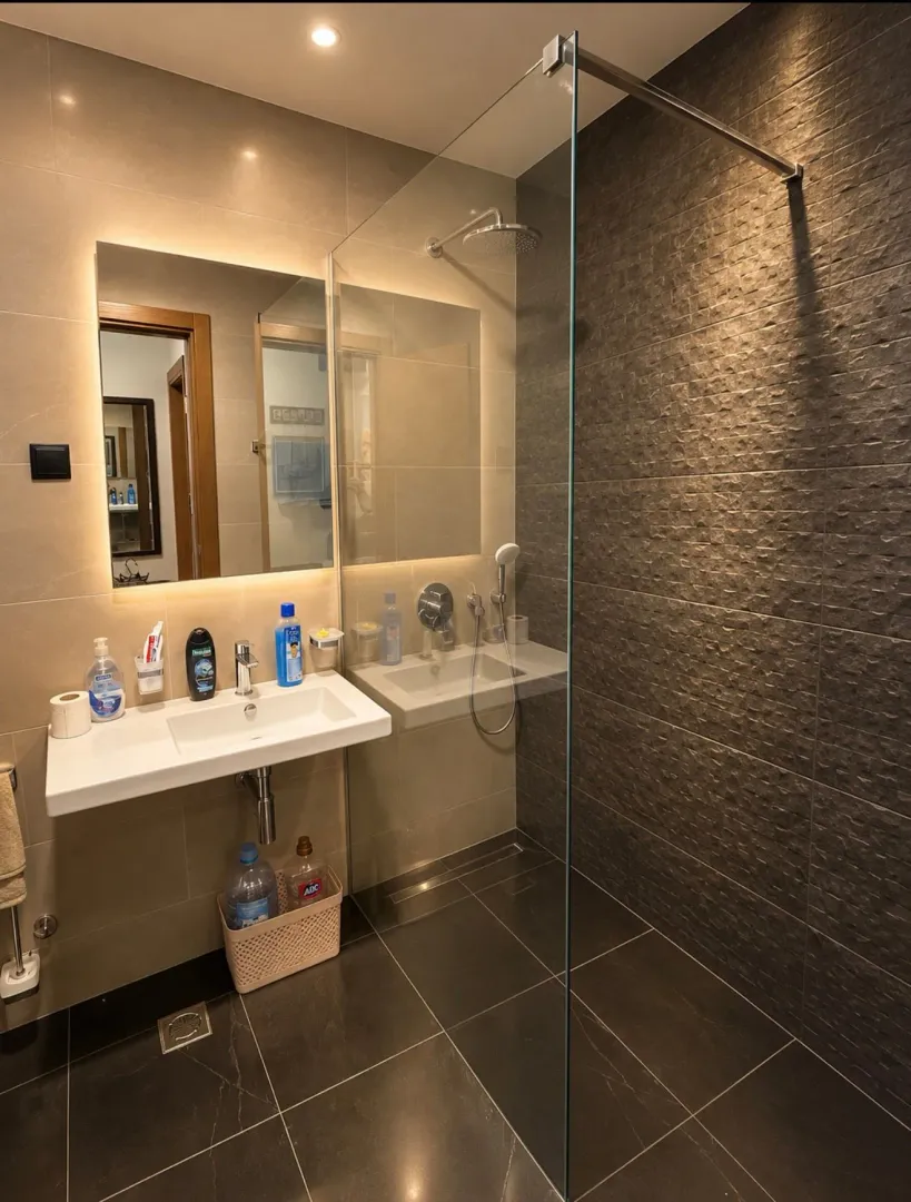Modern bathroom with a sink, illuminated mirror, and a glass shower cabin.