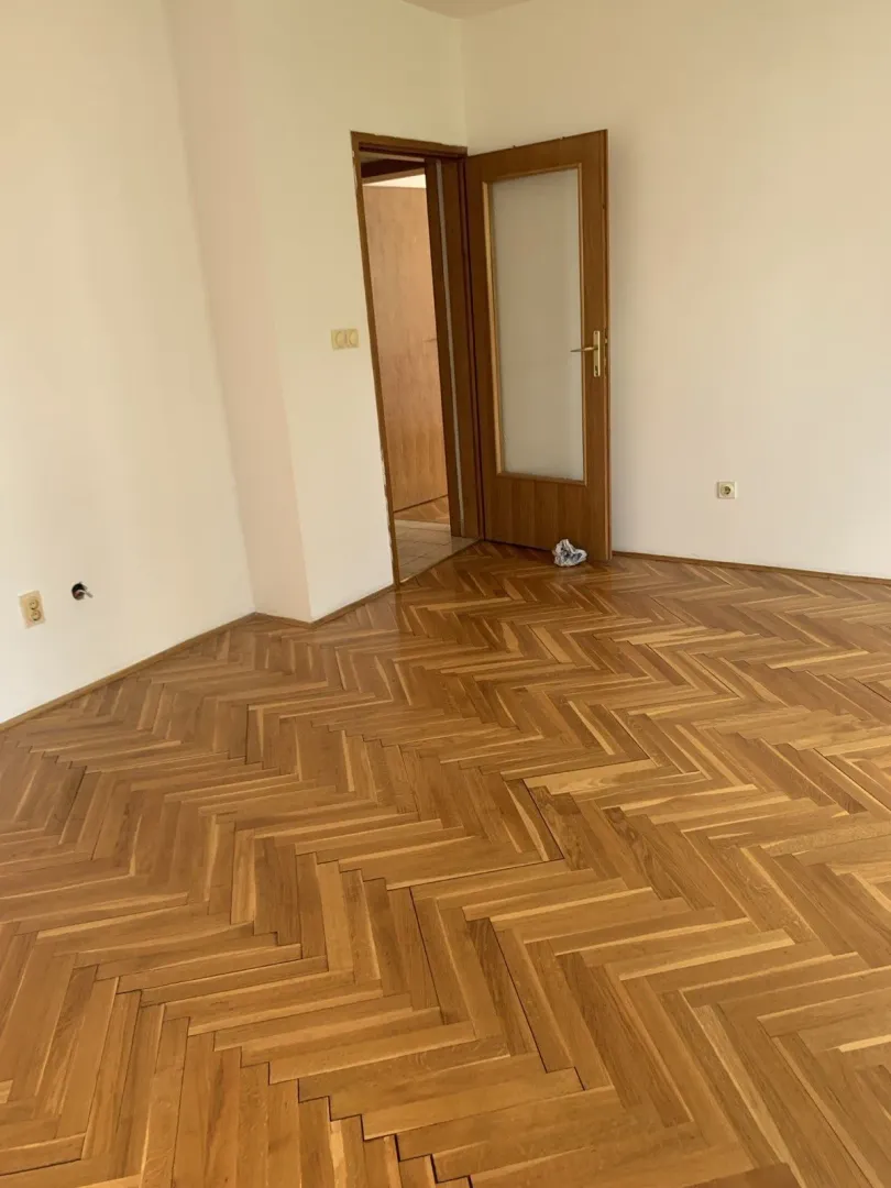 Prazna soba sa očuvanim parketom i drvenim vratima.
