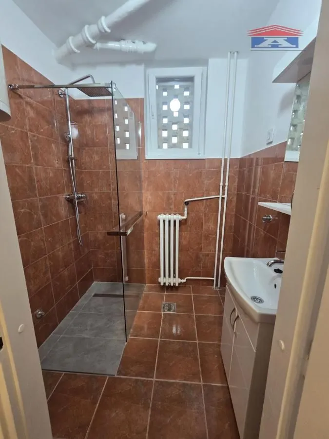 Kupatilo sa tuš kabinom obloženo braon pločicama.