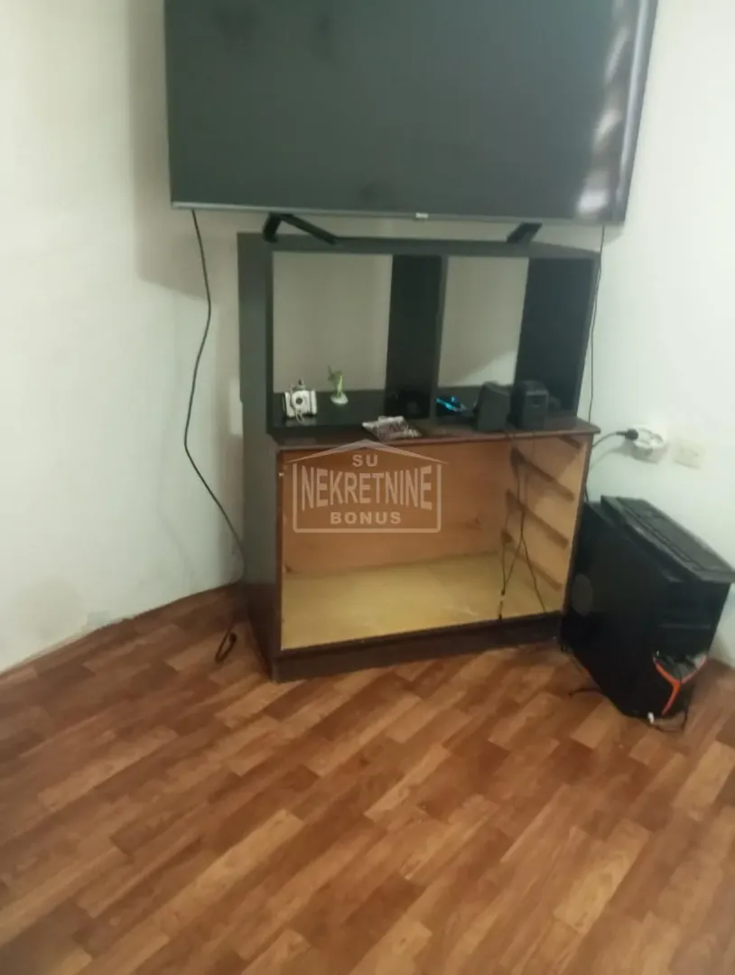 Dnevna soba sa televizorom postavljenom na komodu i laminatom na podu.