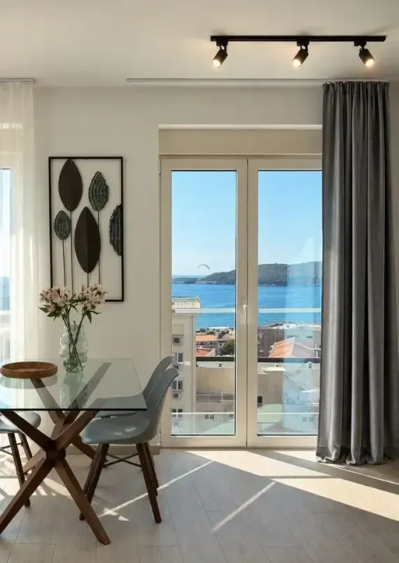 Trpezarija sa staklenim stolom i pogledom na more kroz balkonska vrata.