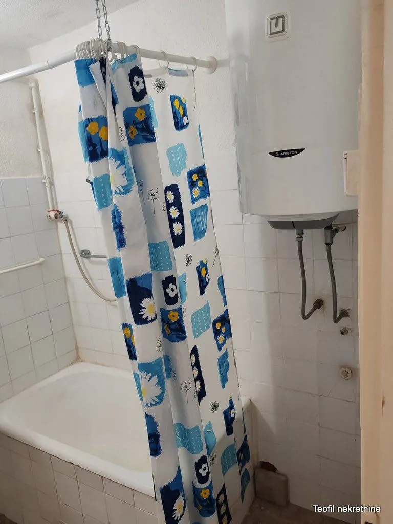 Manje kupatilo sa kadom, zavesom za tuš i bojlerom na zidu.
