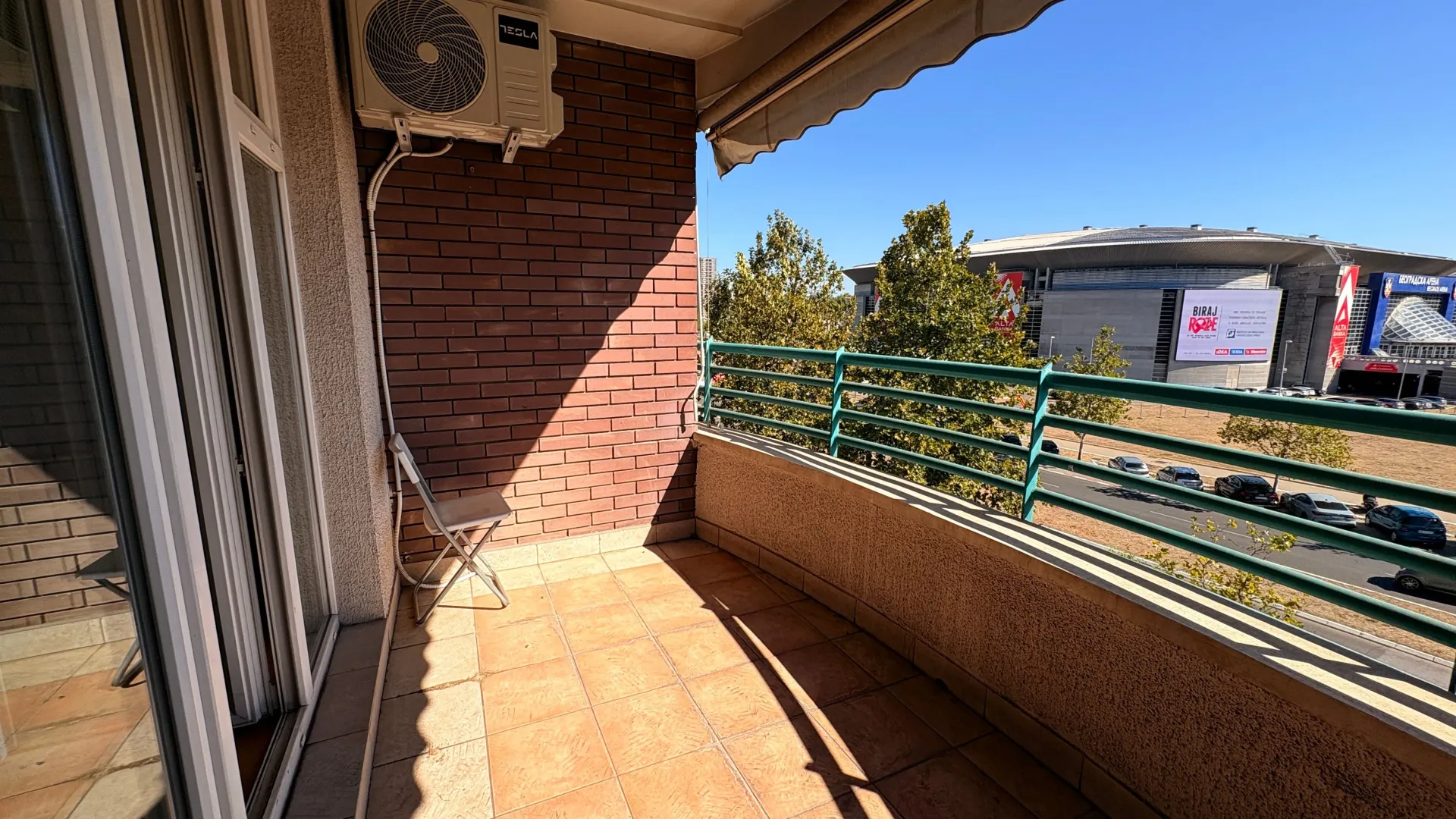 Spacious balcony with a city view and an air conditioning unit on the wall.