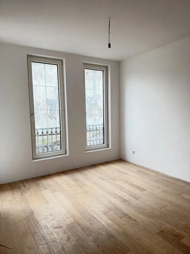 Empty unfinished room with wooden flooring and two windows.