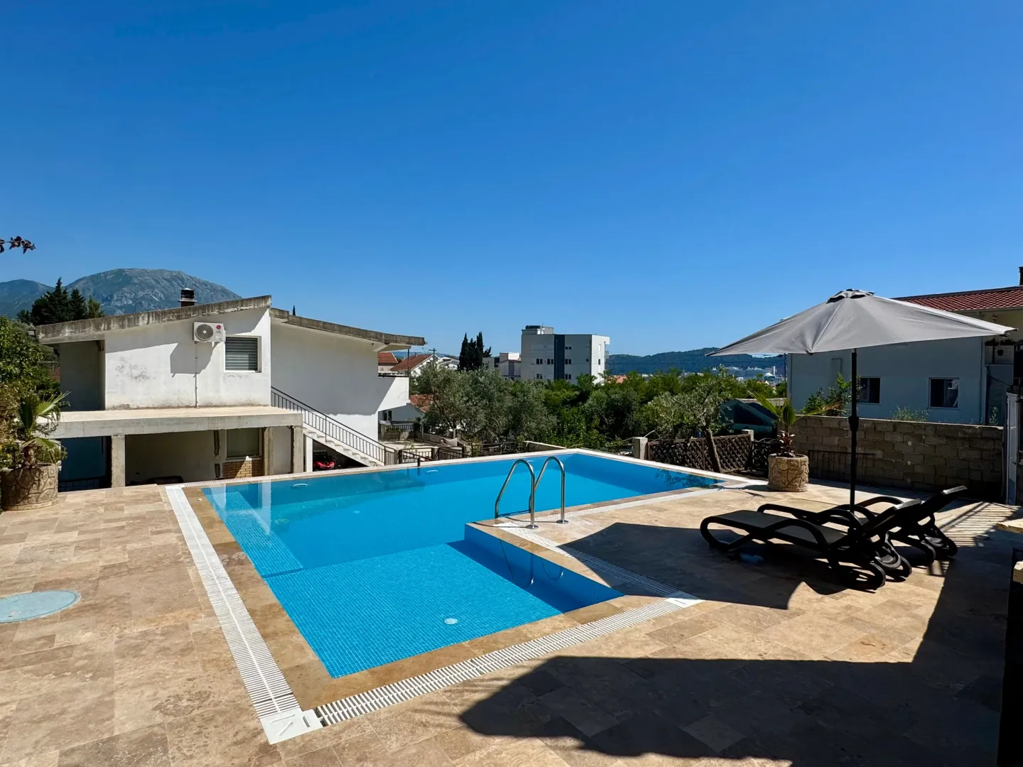 Swimming pool with a sunny terrace, loungers, and an umbrella in the house yard.