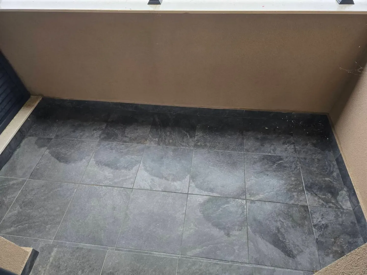 View of a small unfurnished balcony with dark ceramic tiles.