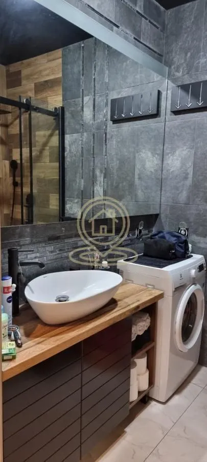 Modern bathroom with a washbasin on a wooden vanity, a mirror, and a washing machine.