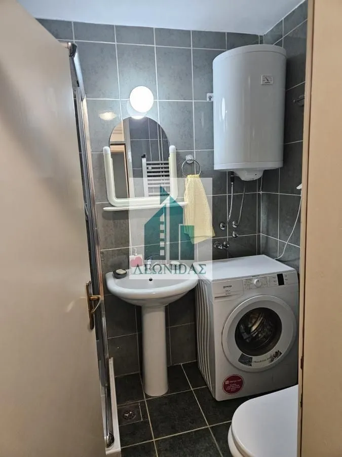 Small bathroom with a sink, shower cabin, washing machine, and water heater.