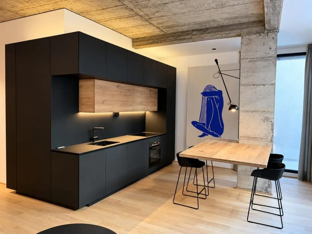 Modern black kitchen with wooden accents and a dining table with bar stools.