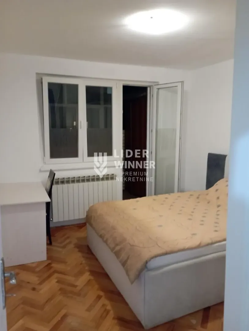 Nameštena spavaća soba sa bračnim krevetom, radnim stolom i izlazom na terasu.