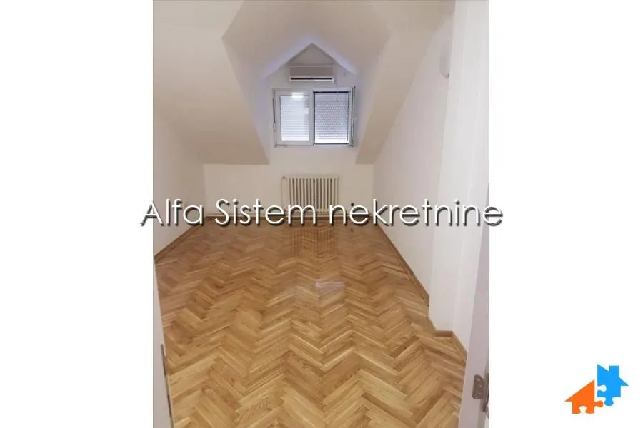 Prazna potkrovna soba sa parketom na podu i prozorom.