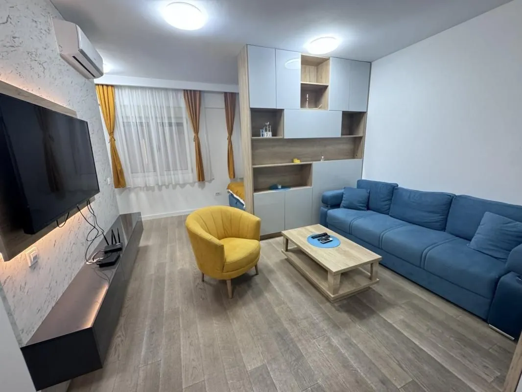 Dnevni boravak sa plavom garniturom, žutom foteljom i TV komodom.