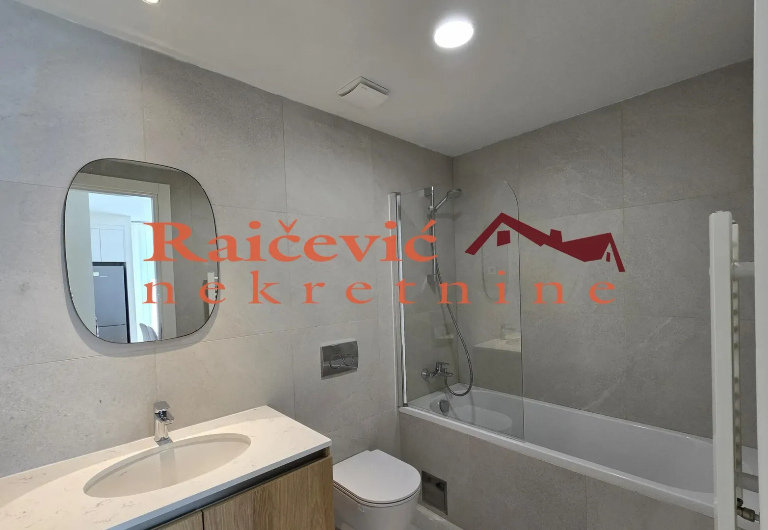 Modern bathroom with a washbasin, mirror, toilet, and bathtub with a glass partition.
