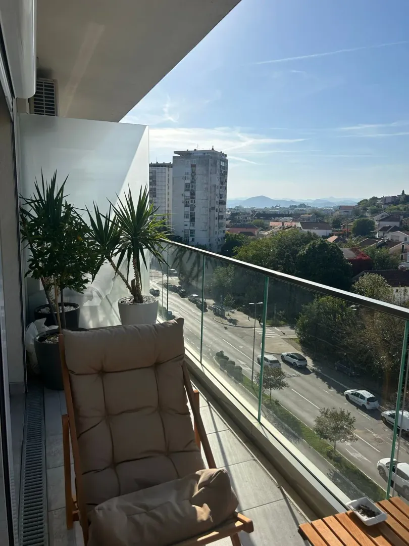 Namješten balkon sa staklenom ogradom i pogledom na gradsku ulicu.