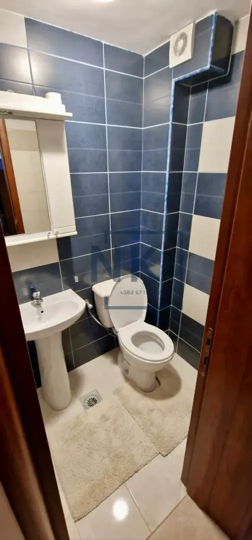 Manje kupatilo sa plavim i bijelim pločicama, umivaonikom i wc šoljom.