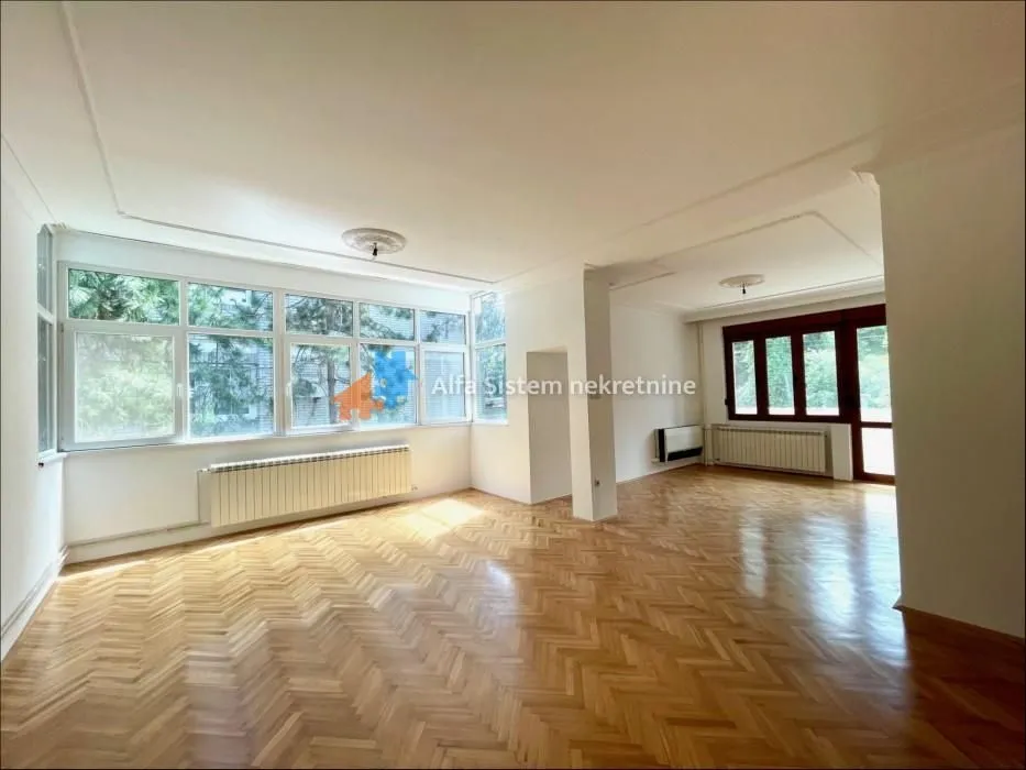 Spacious bright living room with large windows and parquet flooring.