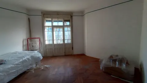 Prazna soba sa drvenim podom, velikim dvokrilnim vratima i krevetom prekrivenim zaštitnom folijom. - image 12