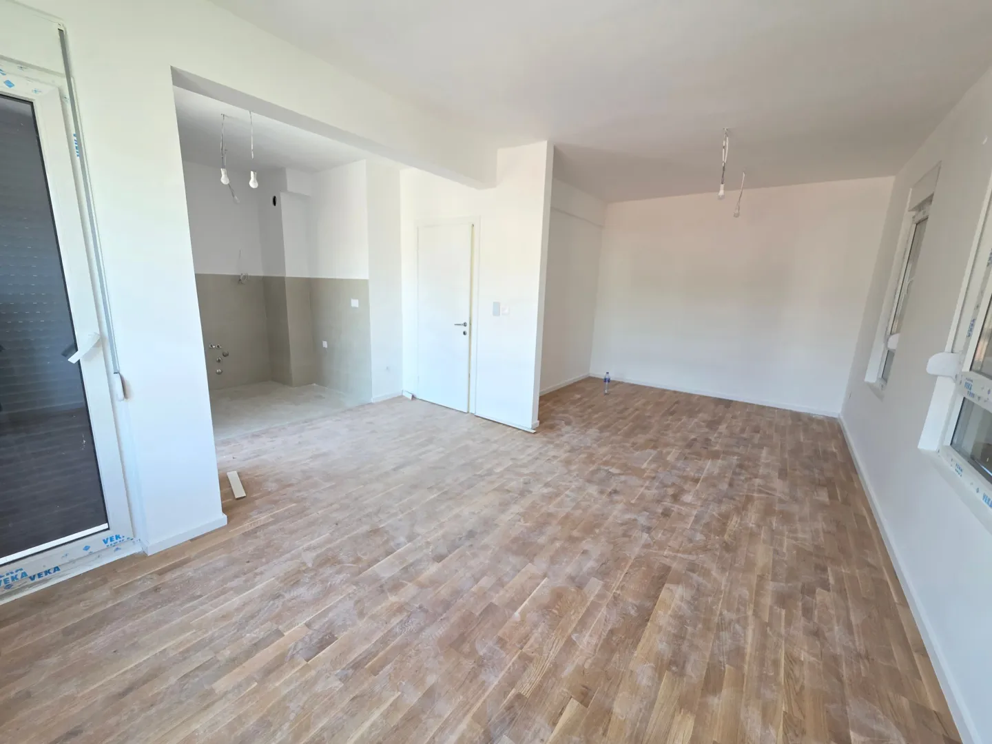 Empty room with hardwood flooring and white walls under renovation.