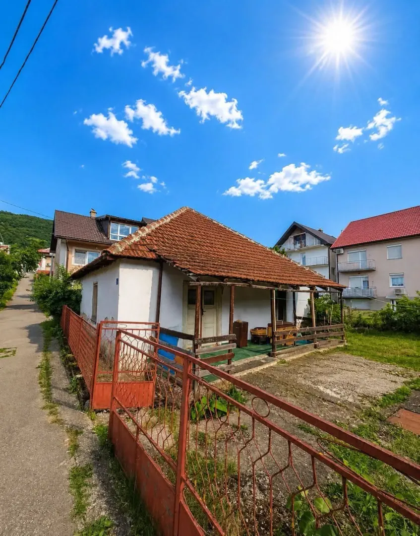 Pogled na stariju prizemnu kuću sa dvorištem i ogradom.