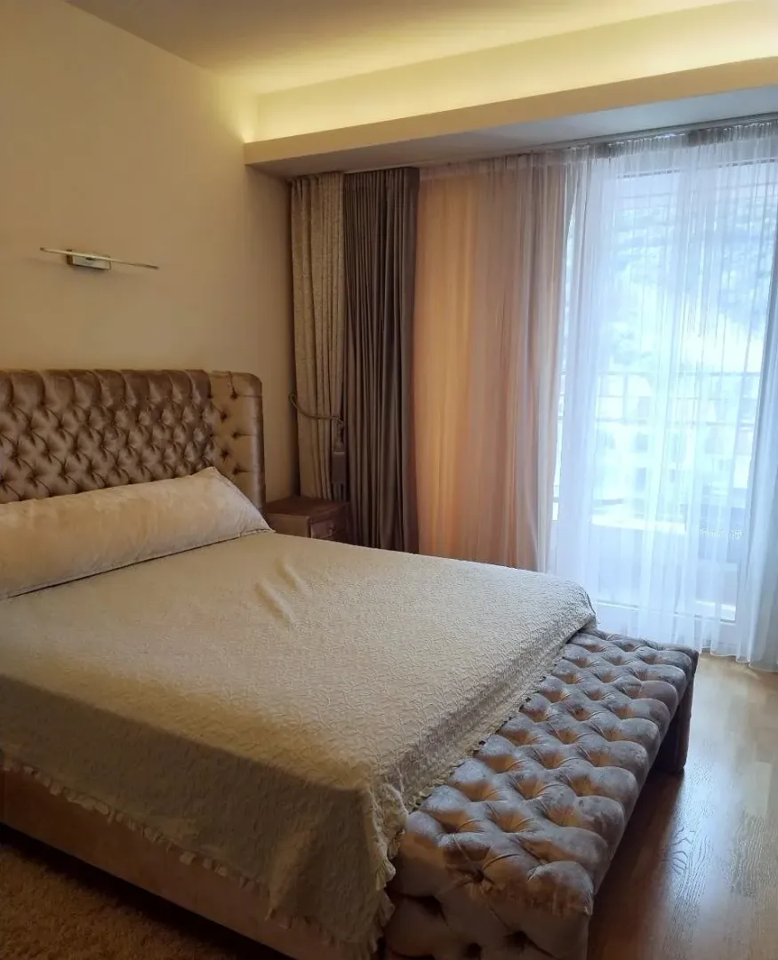 A furnished bedroom with a double bed and a window with curtains.