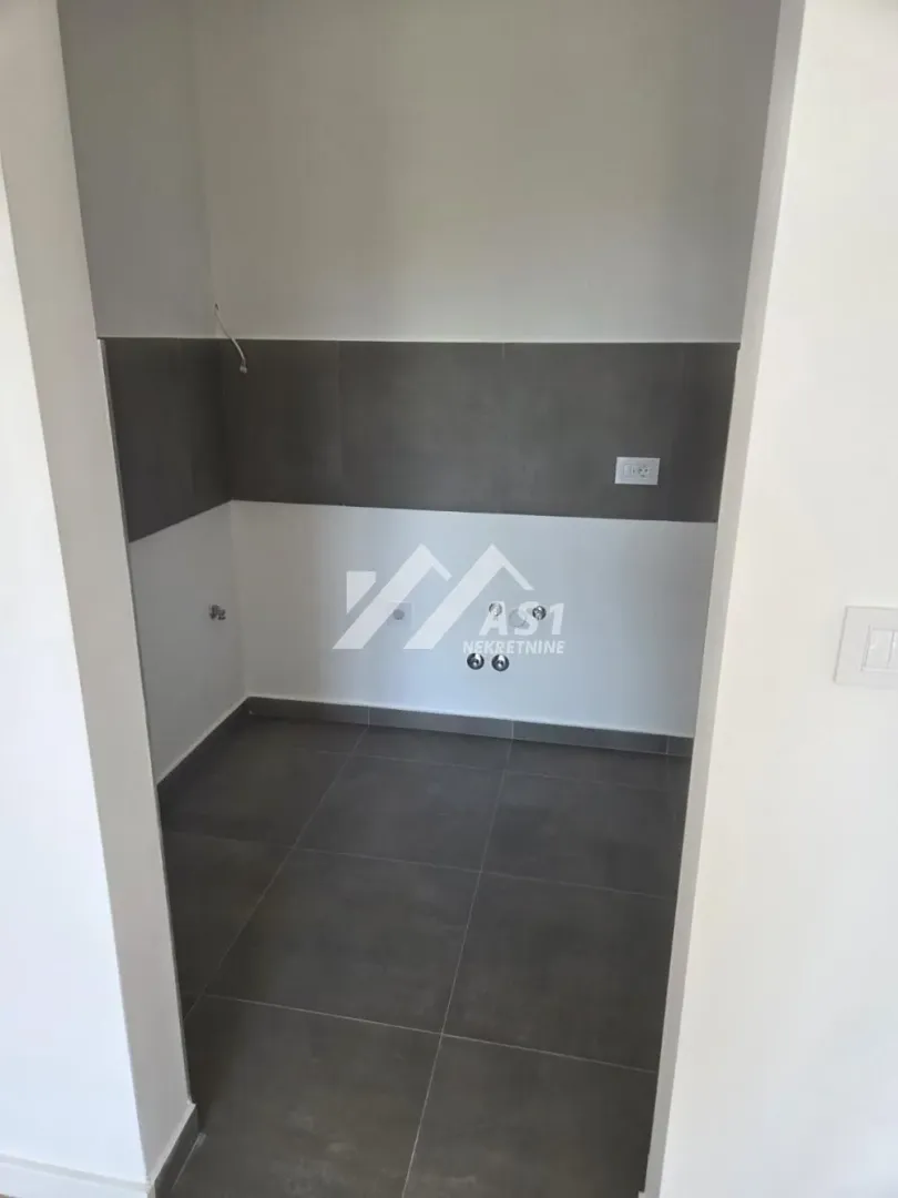 Empty room intended for a kitchen with water and electricity connections.