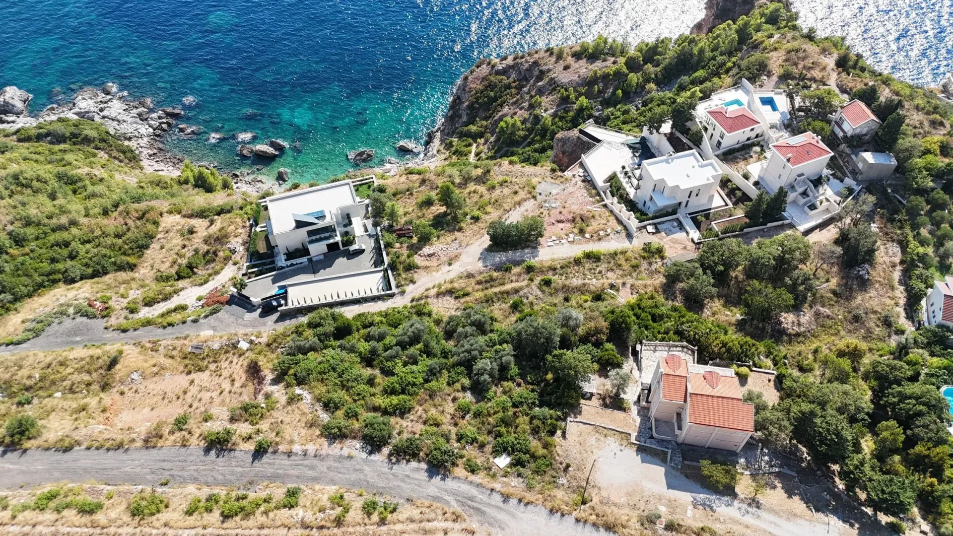 Pogled iz vazduha na kuće smještene na obali mora okružene zelenilom.