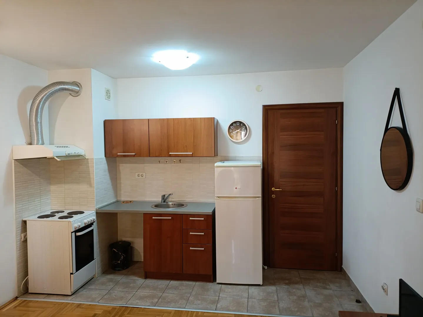 Manja kuhinja sa drvenim elementima, šporetom i frižiderom.