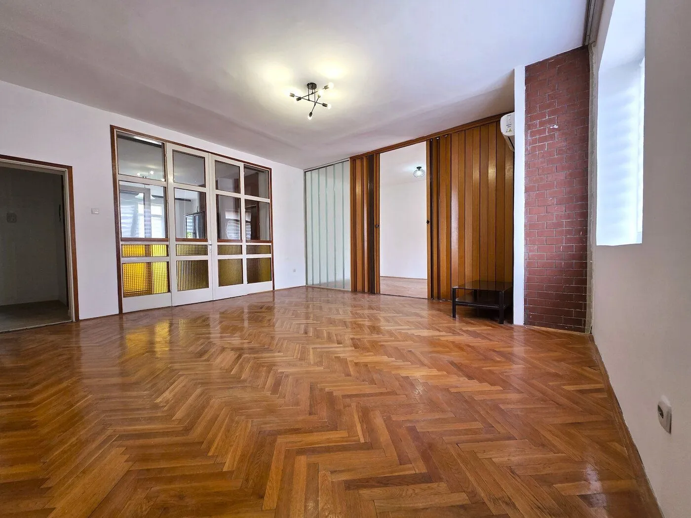 Empty living room with parquet flooring and wooden partition doors.