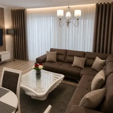 Udobna dnevna soba sa velikom smeđom ugaonom garniturom, staklenim stočićem i elegantnim zavjesama. - image 3
