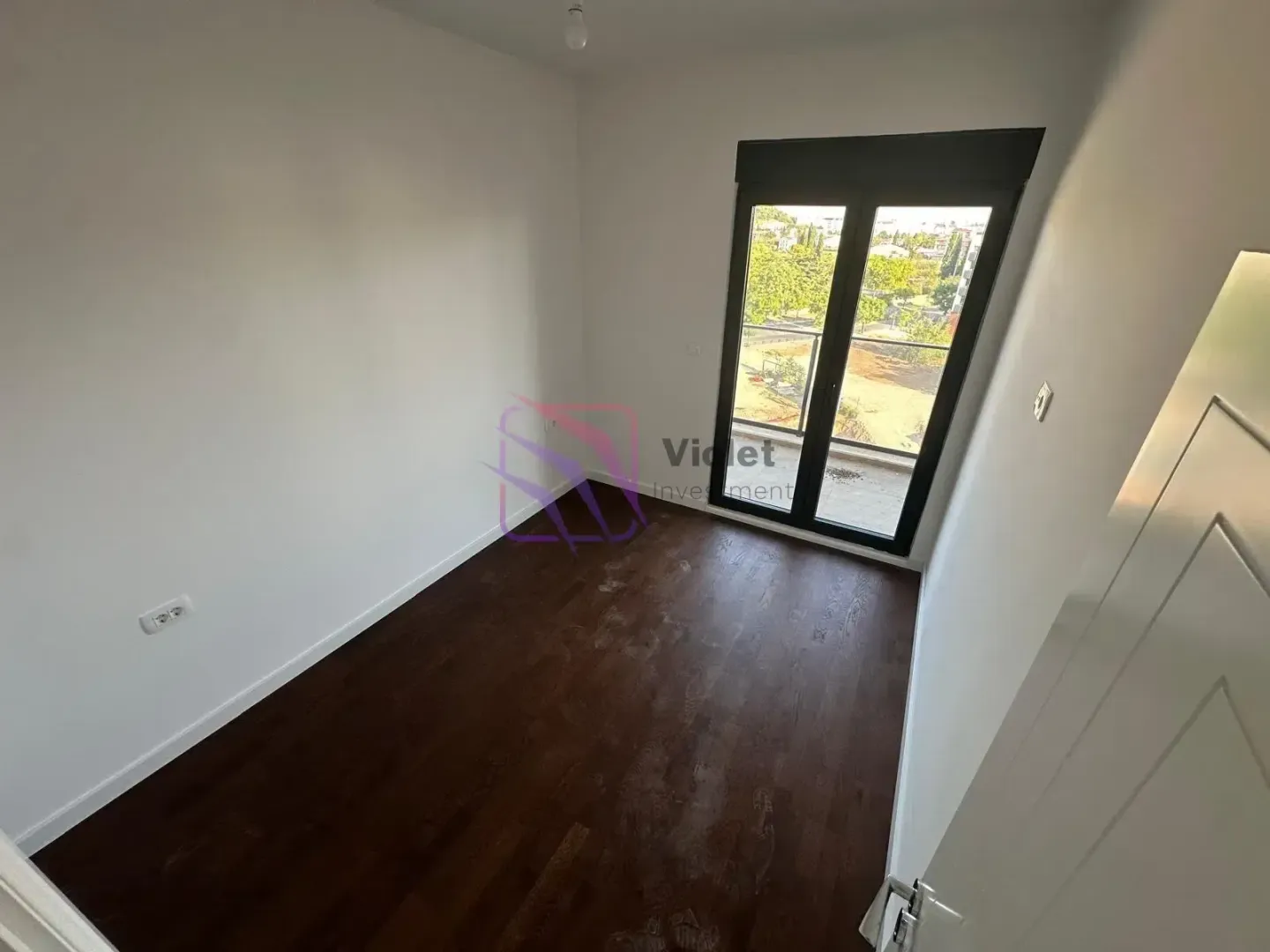 Empty room with dark parquet flooring and balcony doors.