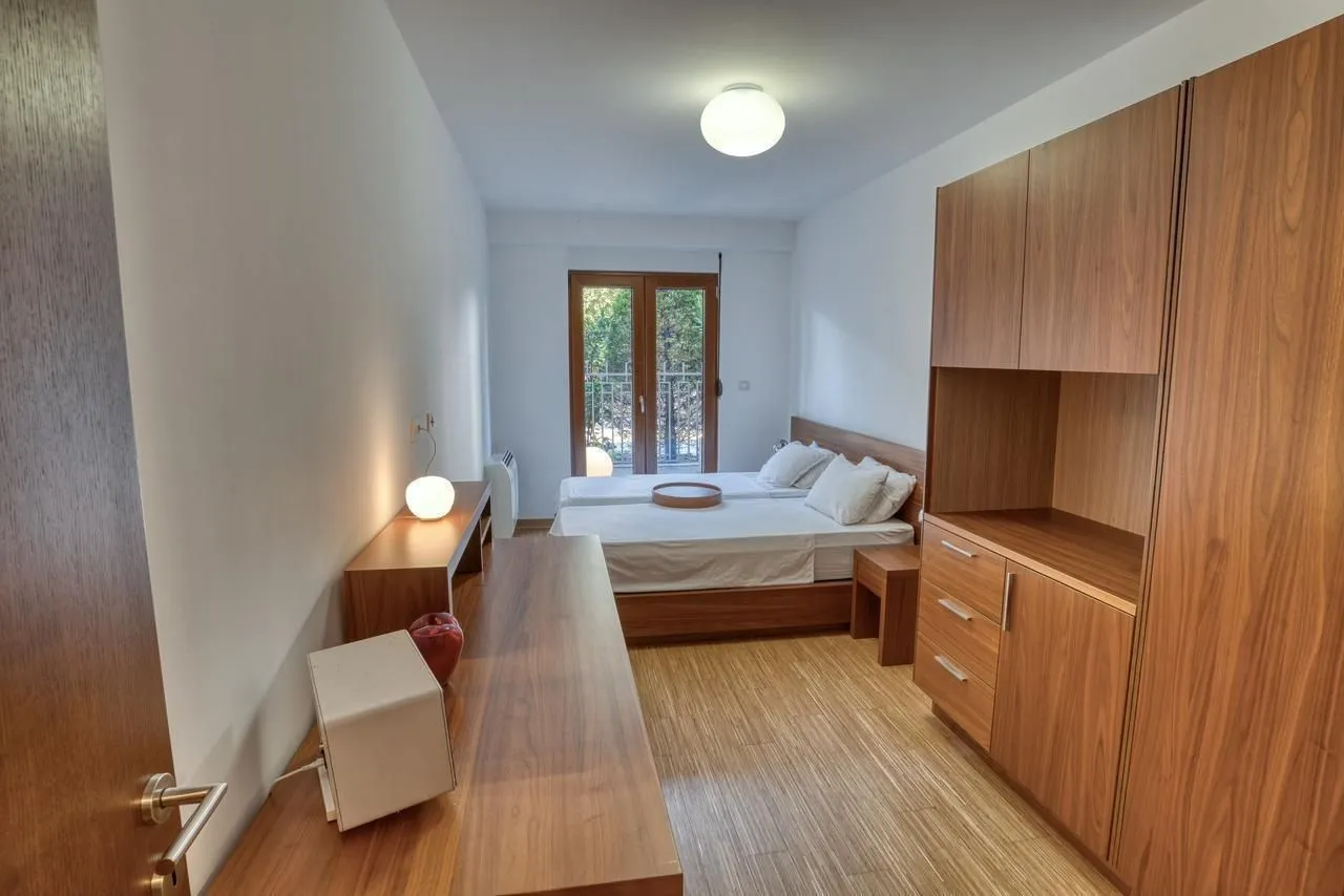 Svijetla spavaća soba sa drvenim namještajem i izlazom na balkon.