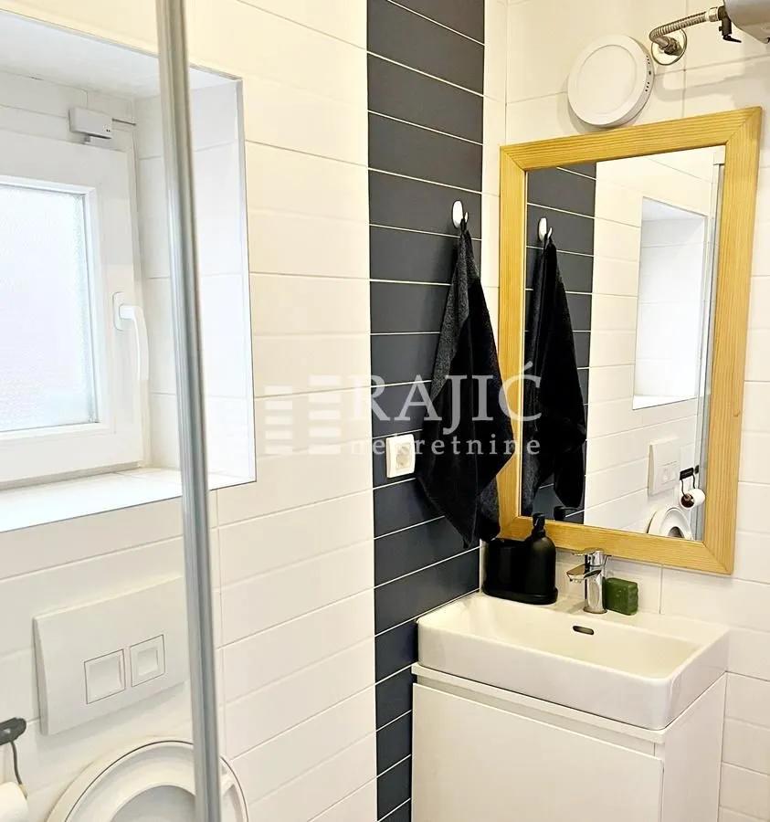 Small modernly decorated bathroom with a sink, mirror, and toilet.