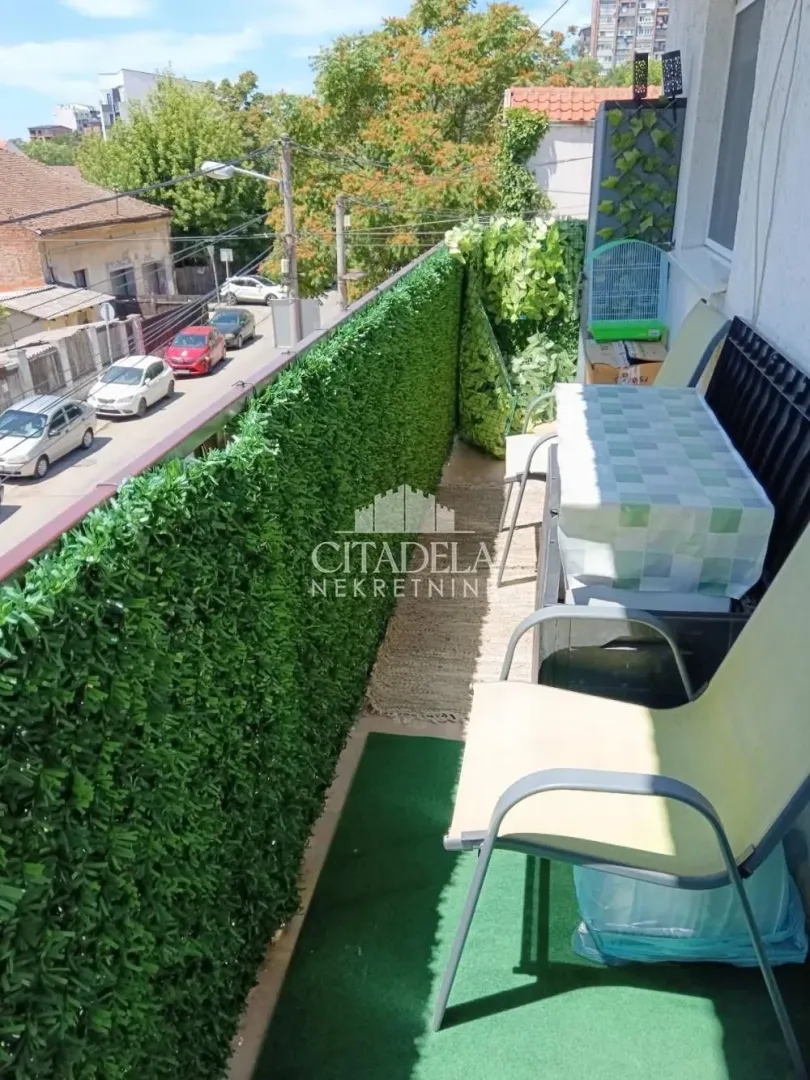 Uski namešteni balkon sa stolom, stolicama i pogledom na ulicu.