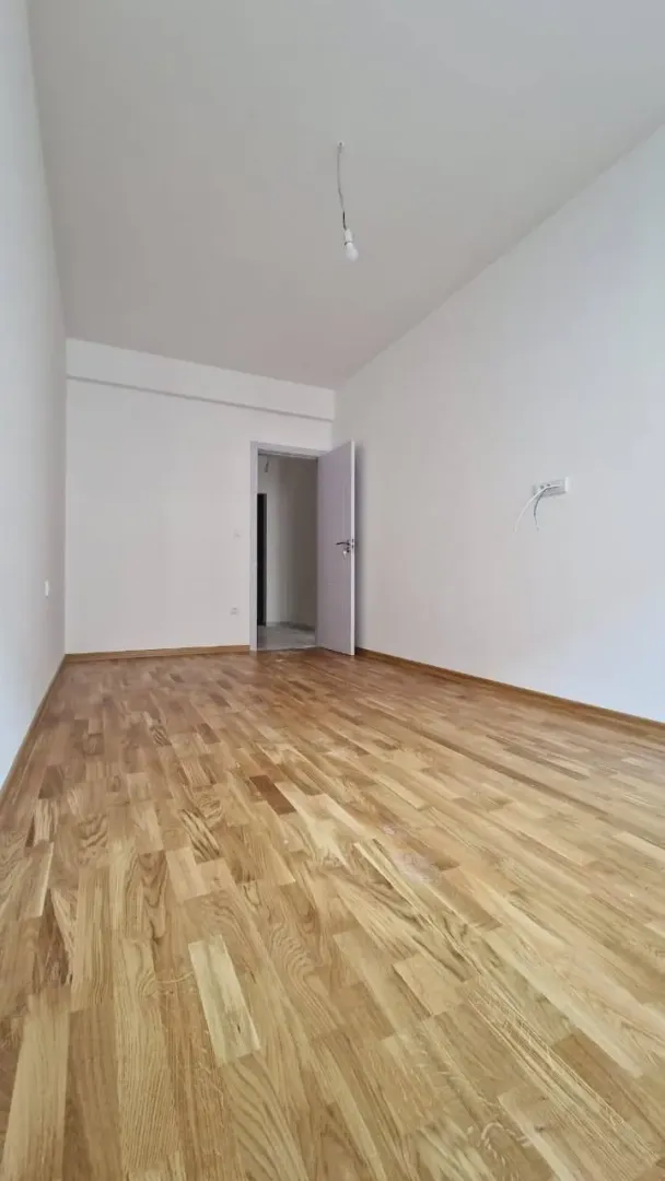 Prazna neopremljena soba sa parketom na podu i bijelim zidovima.