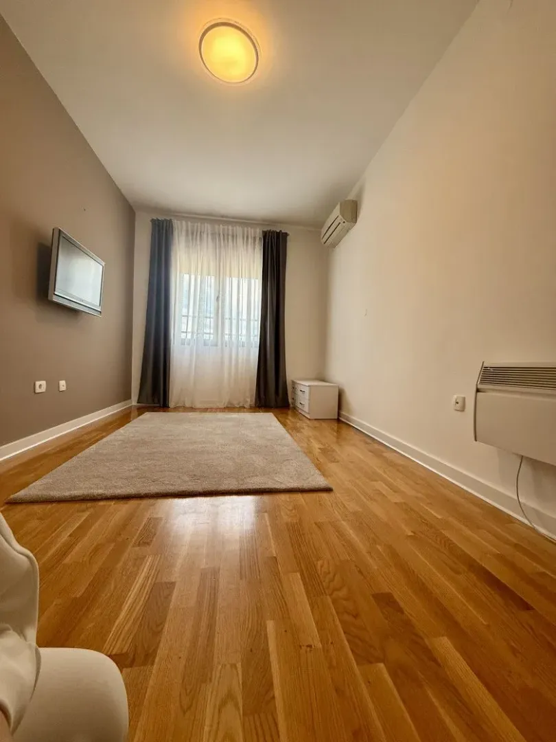 Empty living room with hardwood floors, a rug, and a window.