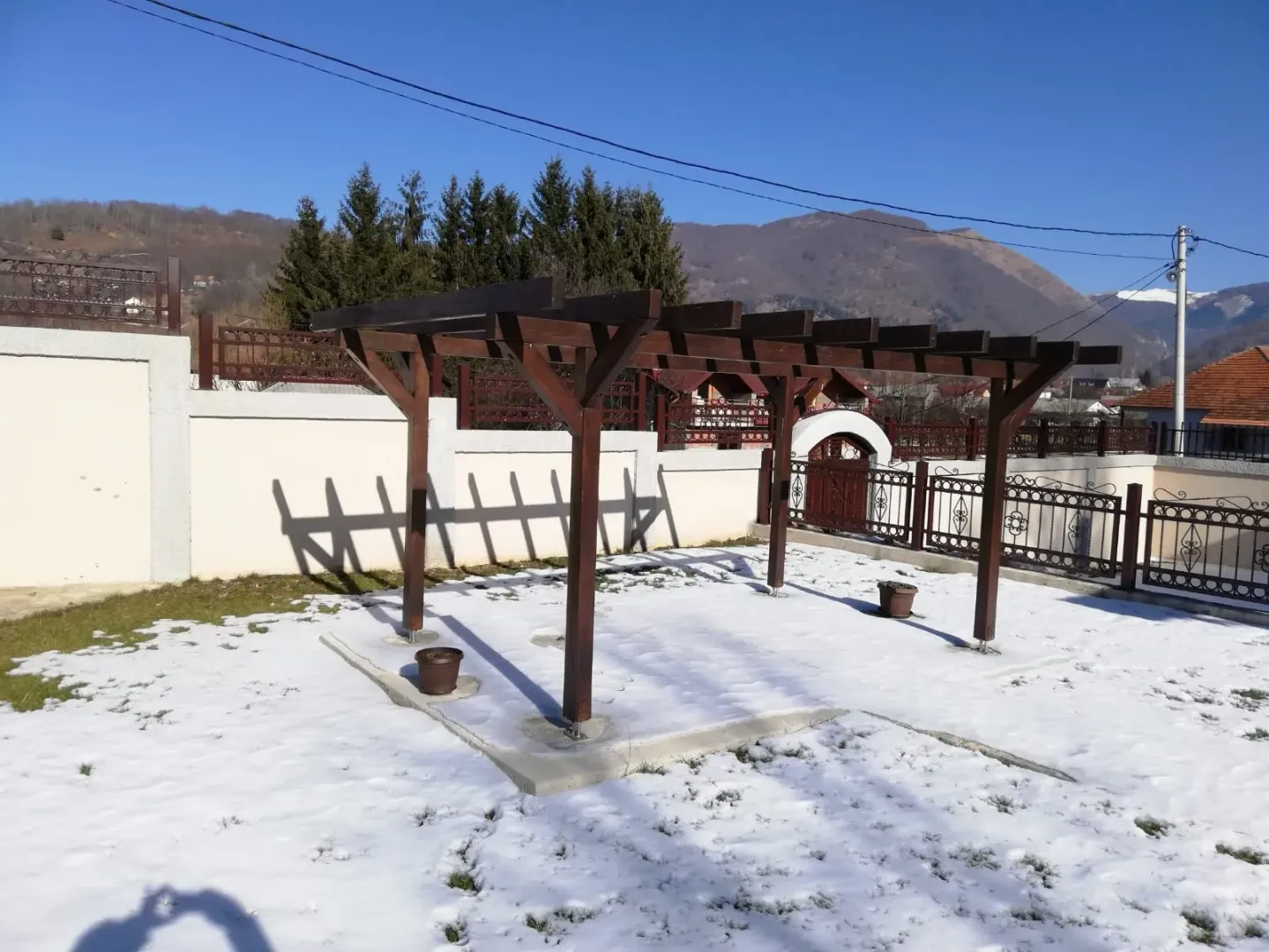 Drvena pergola u dvorištu prekrivenom snijegom sa pogledom na okolne planine.