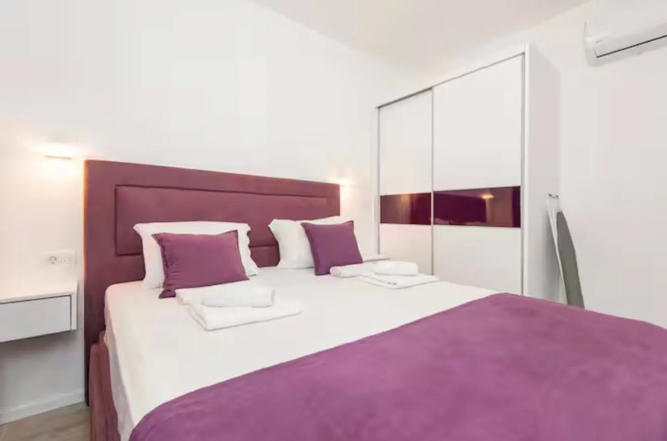 Bright bedroom with a double bed, white wardrobe, and air conditioning.