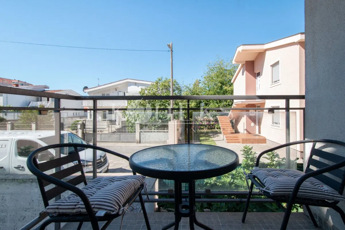 Namješten balkon sa stolom i dve stolice i pogledom na okolne kuće.