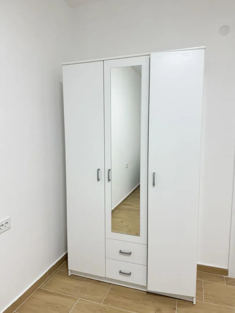 Bijeli garderober sa ogledalom i dvije ladice u sobi sa bijelim zidovima.