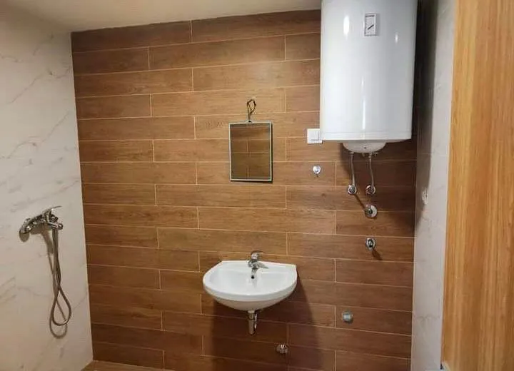Small bathroom with a washbasin, mirror, and water heater on a wood-effect tiled wall.
