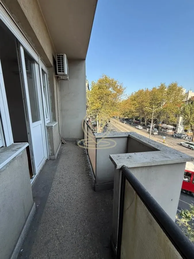 Dugačak balkon sa pogledom na ulicu i drveće.