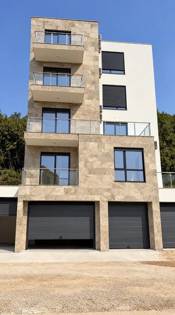 Fasada višestambene zgrade sa terasama i garažama u prizemlju.