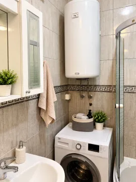 Small bathroom with a shower cabin, washbasin, water heater, and washing machine. - image 7