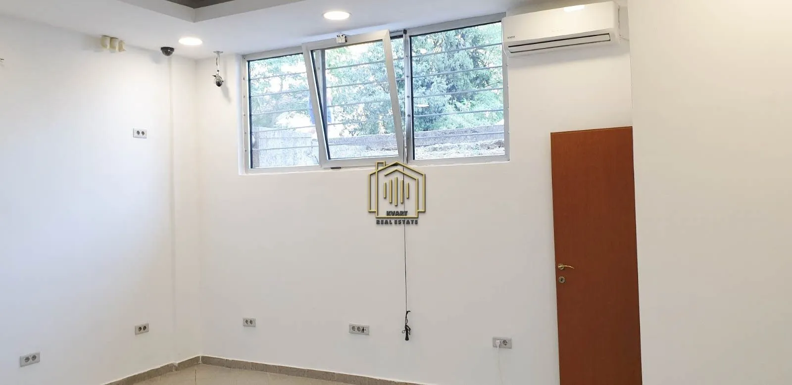 Empty bright room with a window, air conditioning unit, and a wooden door.