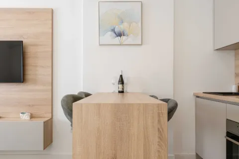 Wooden dining table with chairs and a bottle of wine in the kitchen area. - image 8